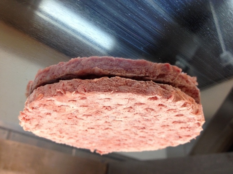 Small burger patties cooking on a metal flat-top griddle
